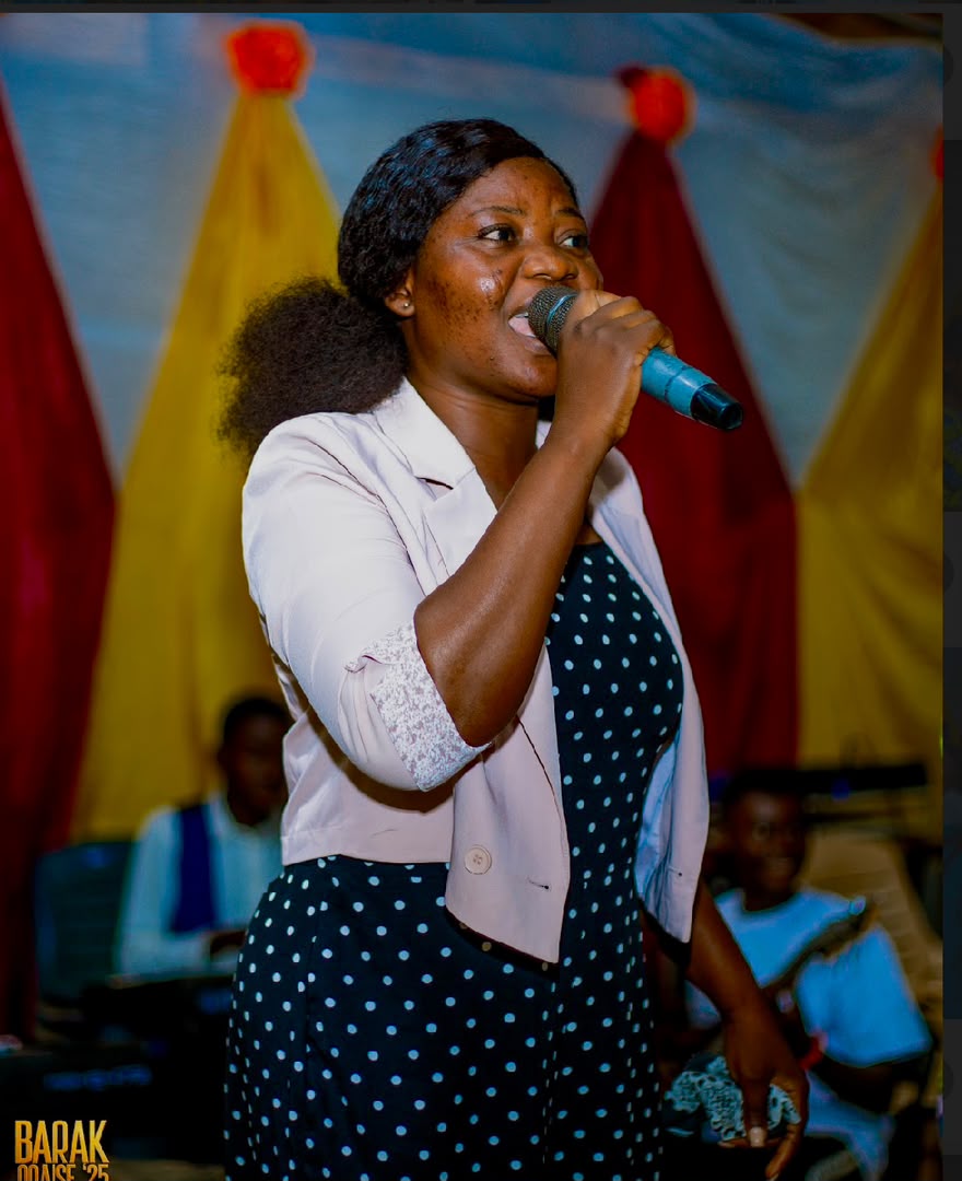 Minister Vida singing into a microphone with the band behind her at Barak Praise 2025.