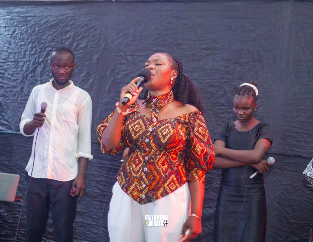 Minister Vida in a printed top leading worship with two backing vocalists at Enthrone Jesus.