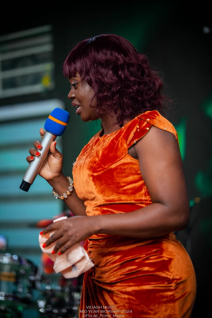 Minister Vida singing under green stage lighting at Mid-Year Worship 2024.