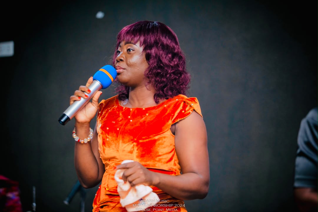 Minister Vida leading worship in an orange velvet dress at Mid-Year Worship 2024.