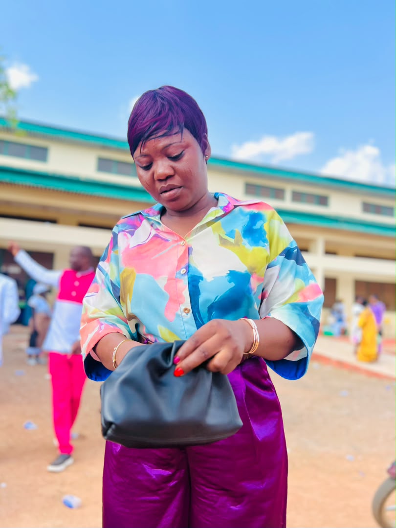 Minister Vida in a printed blouse and purple trousers in a bright courtyard.