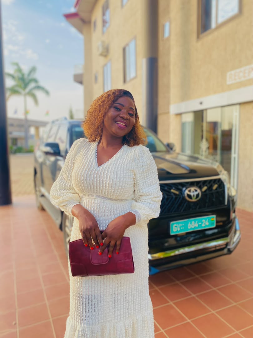Minister Vida in a cream dress holding a maroon clutch outdoors.