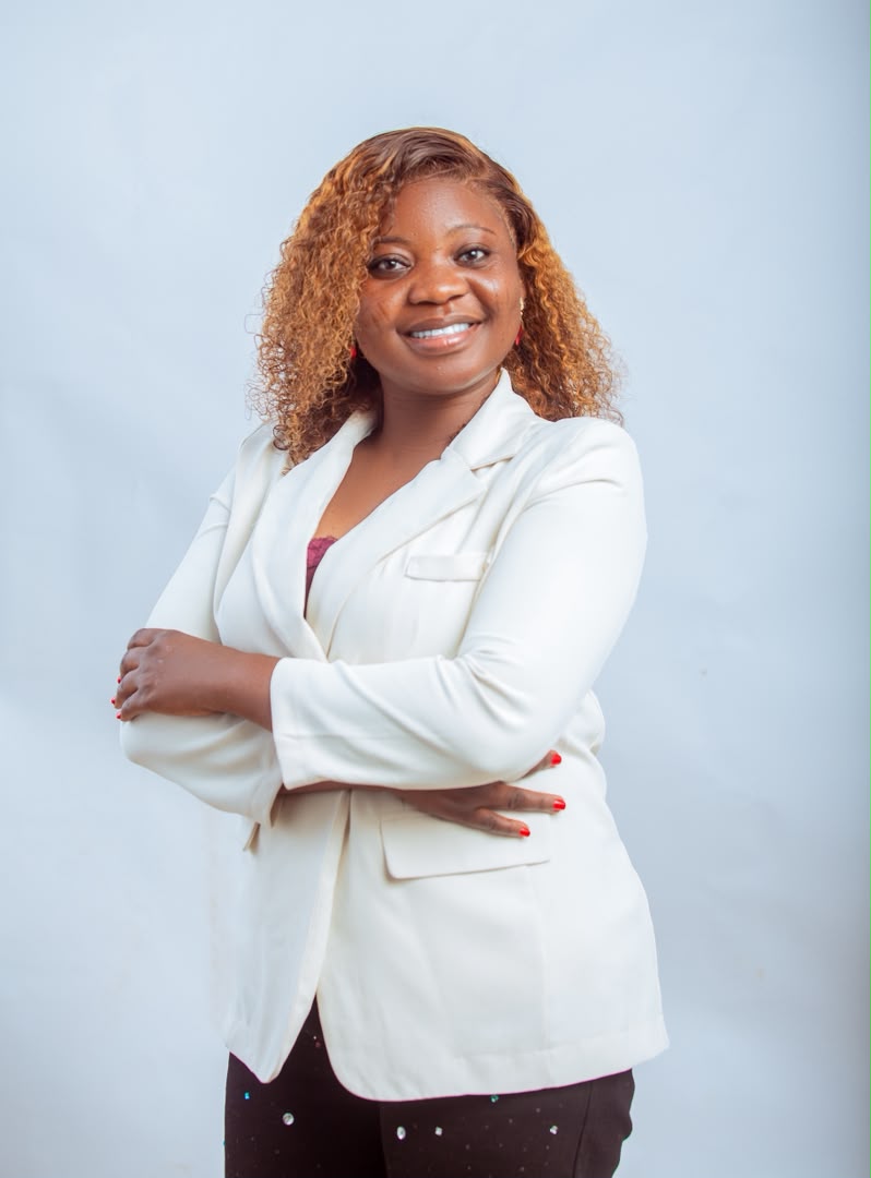 Studio portrait of Minister Vida in a white blazer, arms crossed.